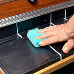 **A person carefully cleaning the inside of an old Dendy console with a soft brush, removing dust.**